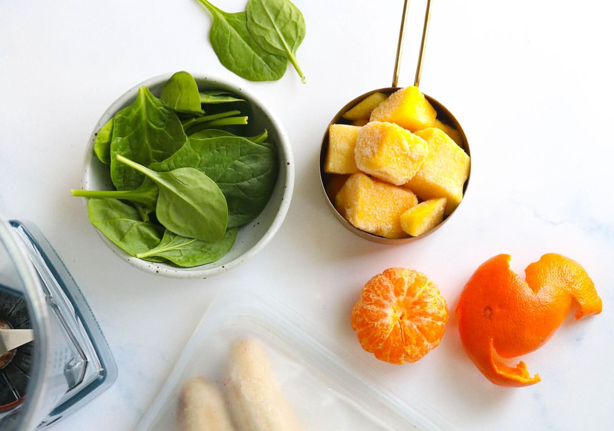 spinach and frozen mango on a white surface