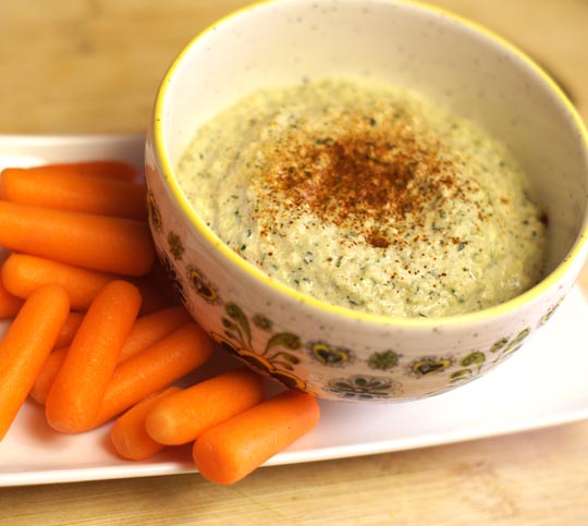 zucchini hummus in a bowl with baby carrots on the side