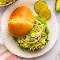 avocado egg salad served on a bun with red onion slices.