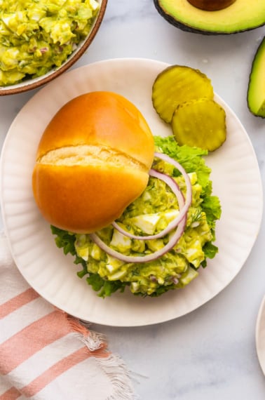 avocado egg salad served on a bun with red onion slices.