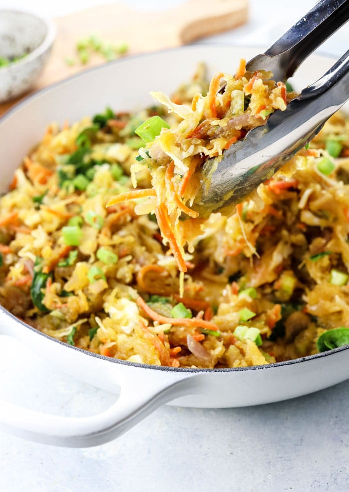 spaghetti squash chow mein in a white skillet with tongs