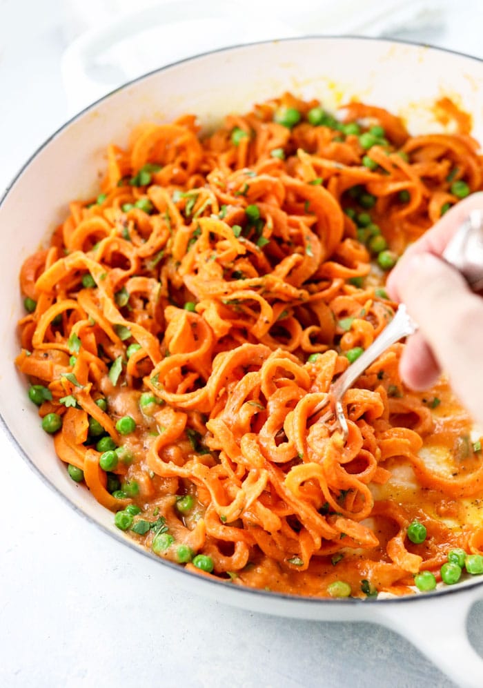 sweet potato noodles in a white skillet with peas