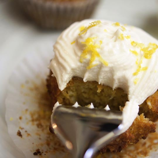 fork taking a piece out of a cupcake with coconut lemon frosting on top
