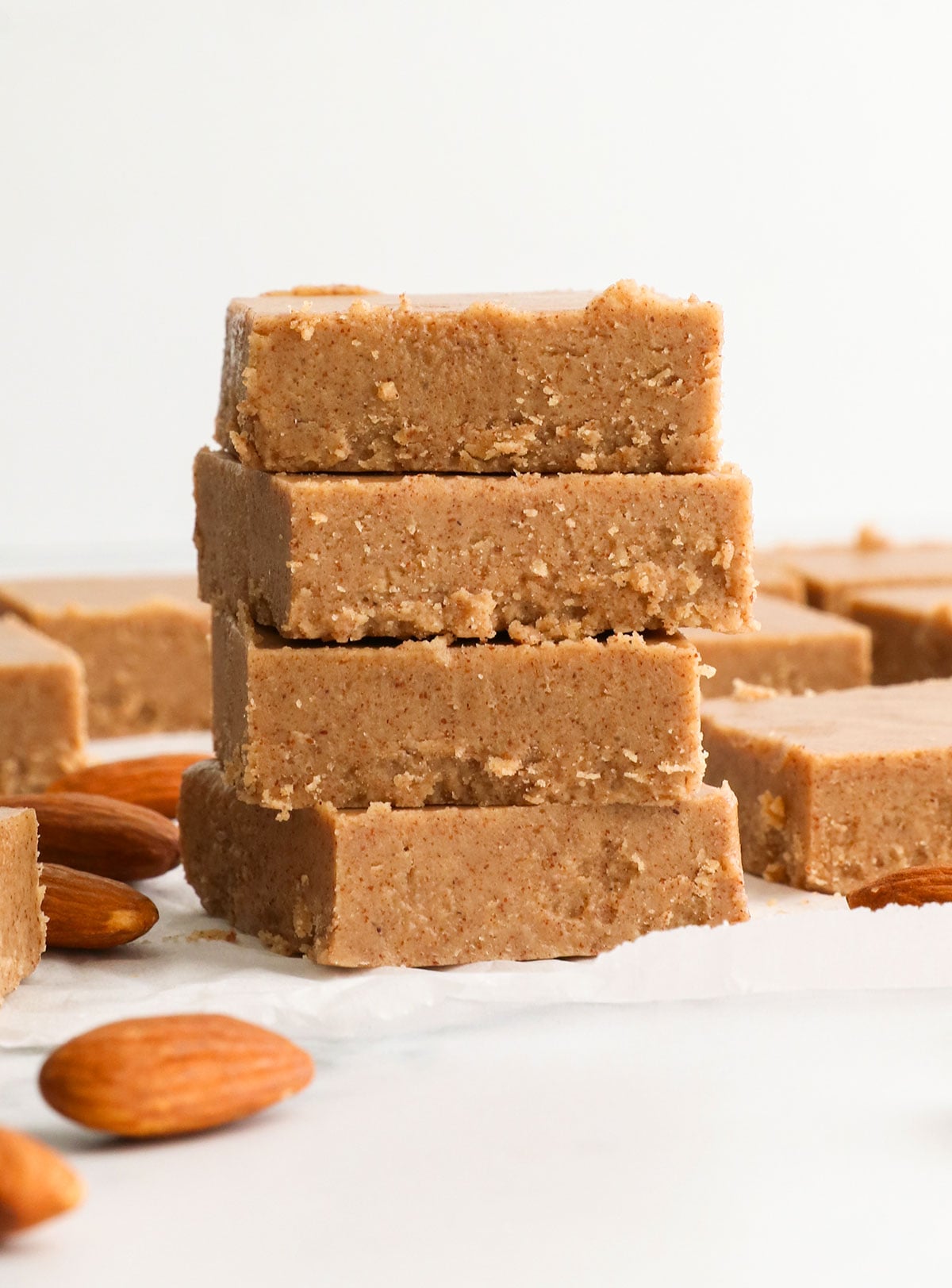 almond butter fudge stacked on a white parchment paper.