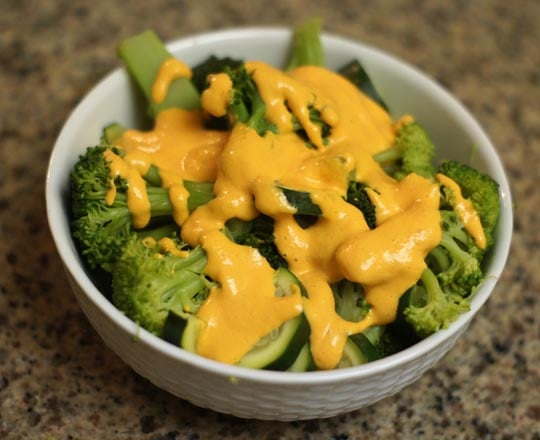 bowl of broccoli with red pepper cheese dip on top