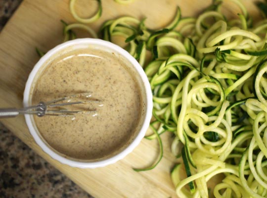 dressing in a small bowl with zucchini noodles next to it