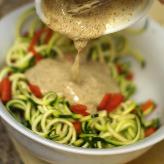 bowl of zucchini noodles with dressing poured on top