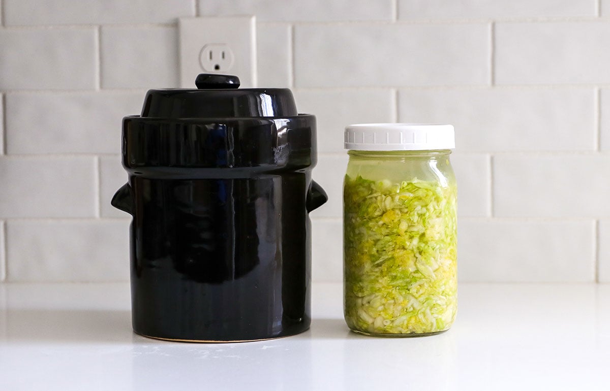 fermentation crock and mason jar of sauerkraut fermenting on the counter. 