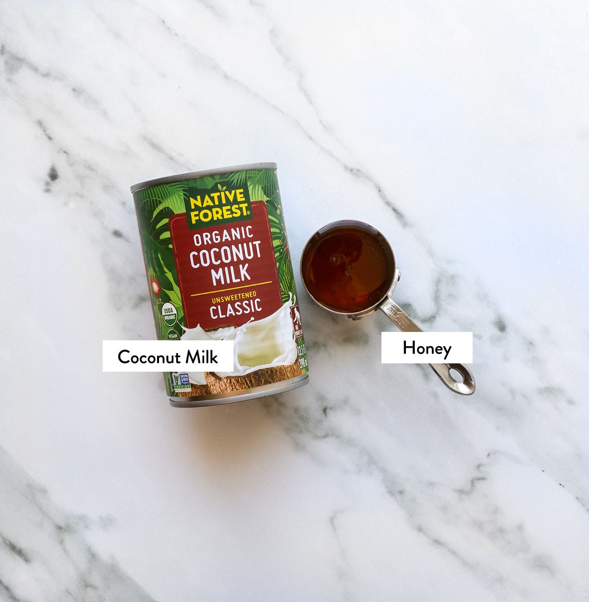canned coconut milk and honey labeled on a marble surface.
