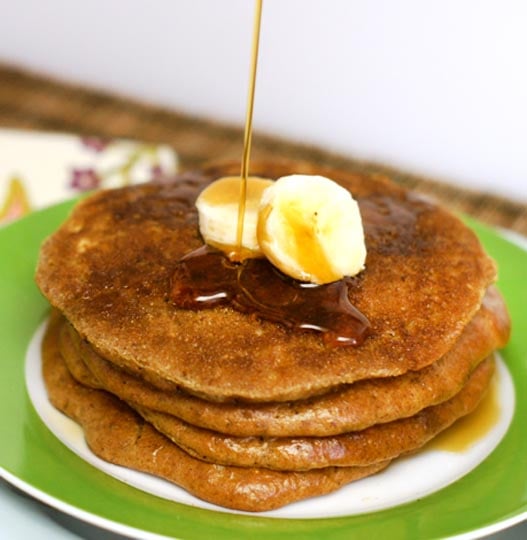 stack of almond butter pancakes on a plate with banana slices and syrup on top