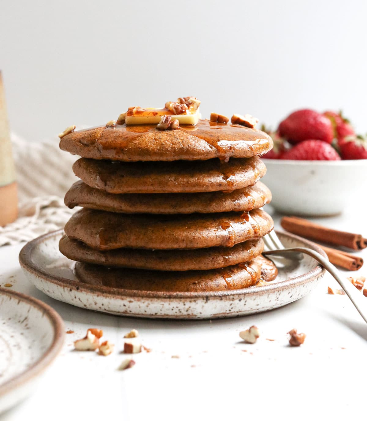 paleo pumpkin pancakes stacked high on a white plate with pecans