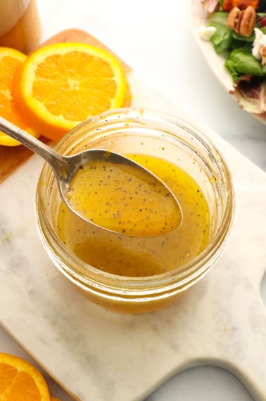 orange dressing lifted up on a spoon over a glass jar.