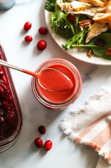 cranberry vinaigrette on a spoon over a jar of dressing.