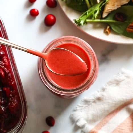 cranberry vinaigrette on a spoon over a jar of dressing.