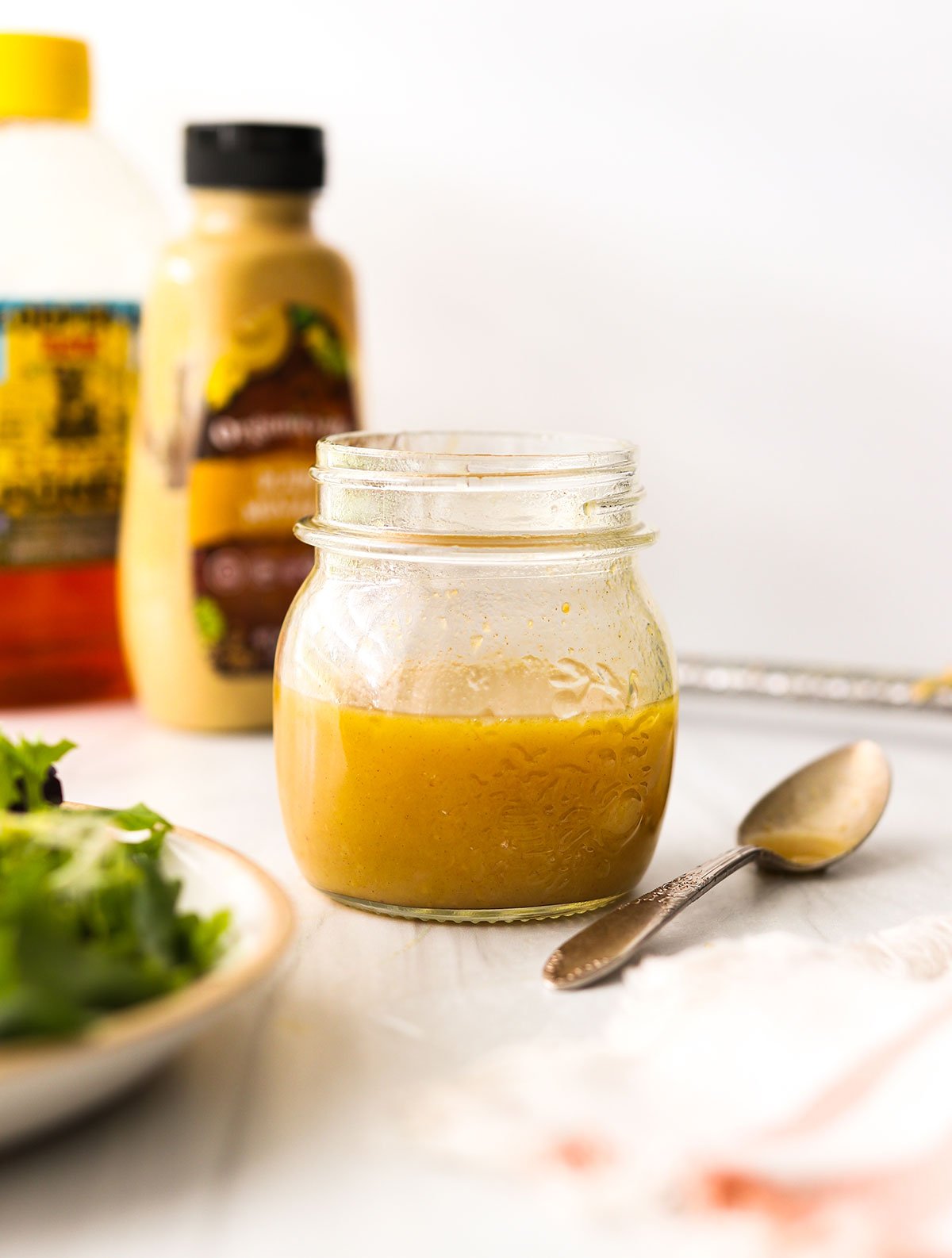 honey dijon salad dressing in a glass jar with a spoon next to it.