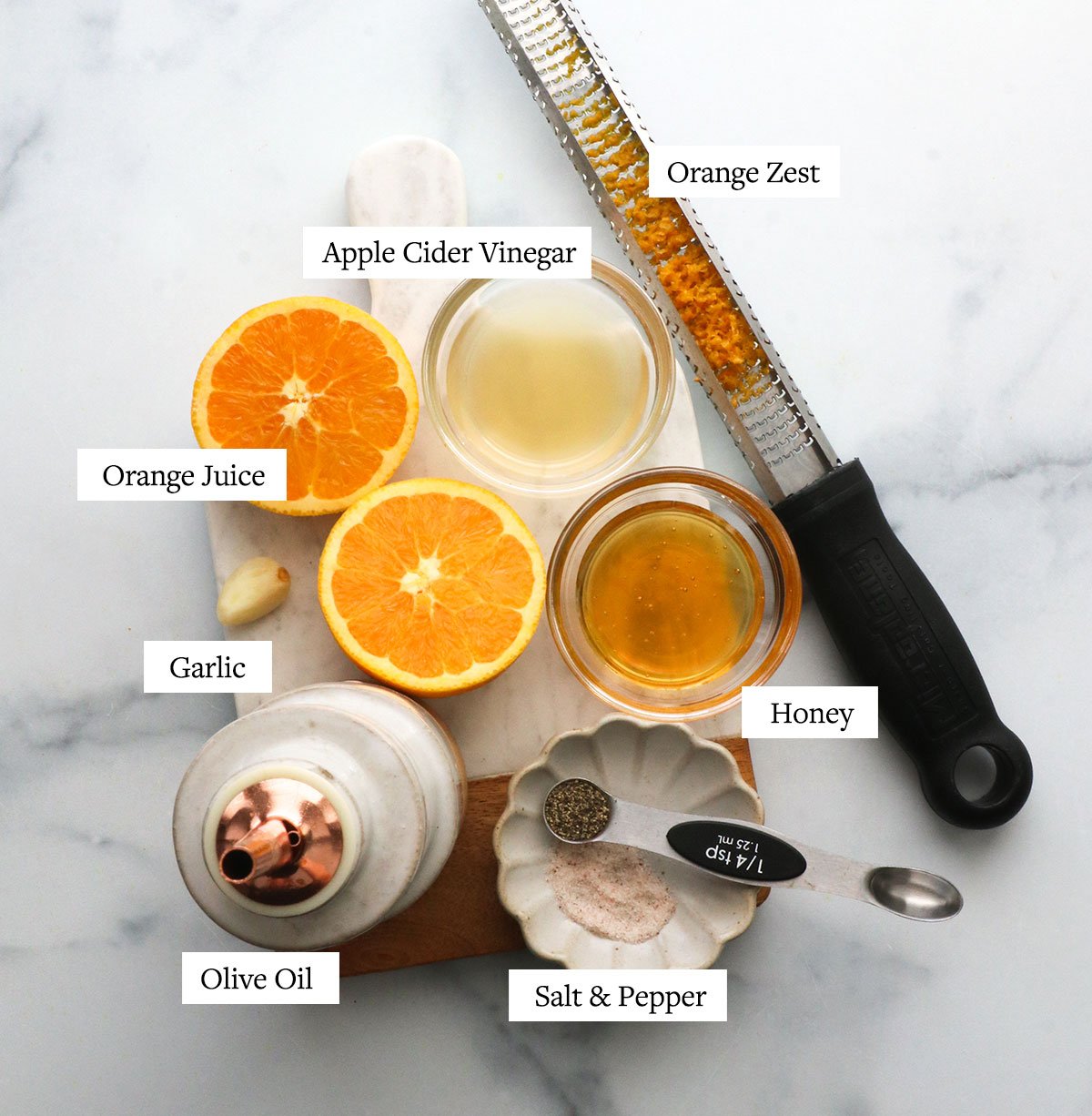 a bottle of olive oil, sliced orange, honey, vinegar, salt and pepper on a marble board.