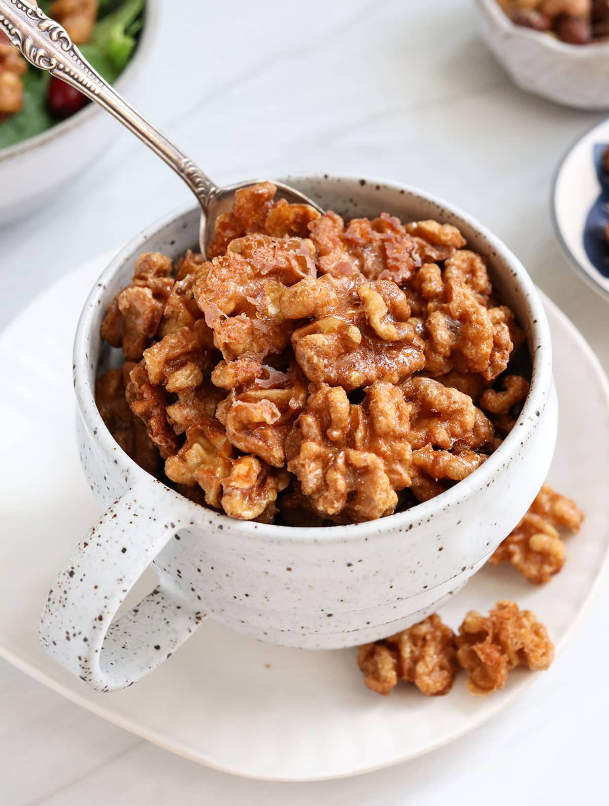 candied walnuts lifted up with a spoon in a mug.
