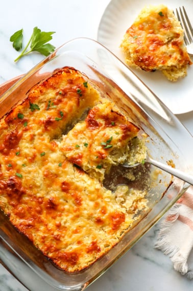 cheesy spaghetti squash casserole in a glass pan near a serving on a plate.