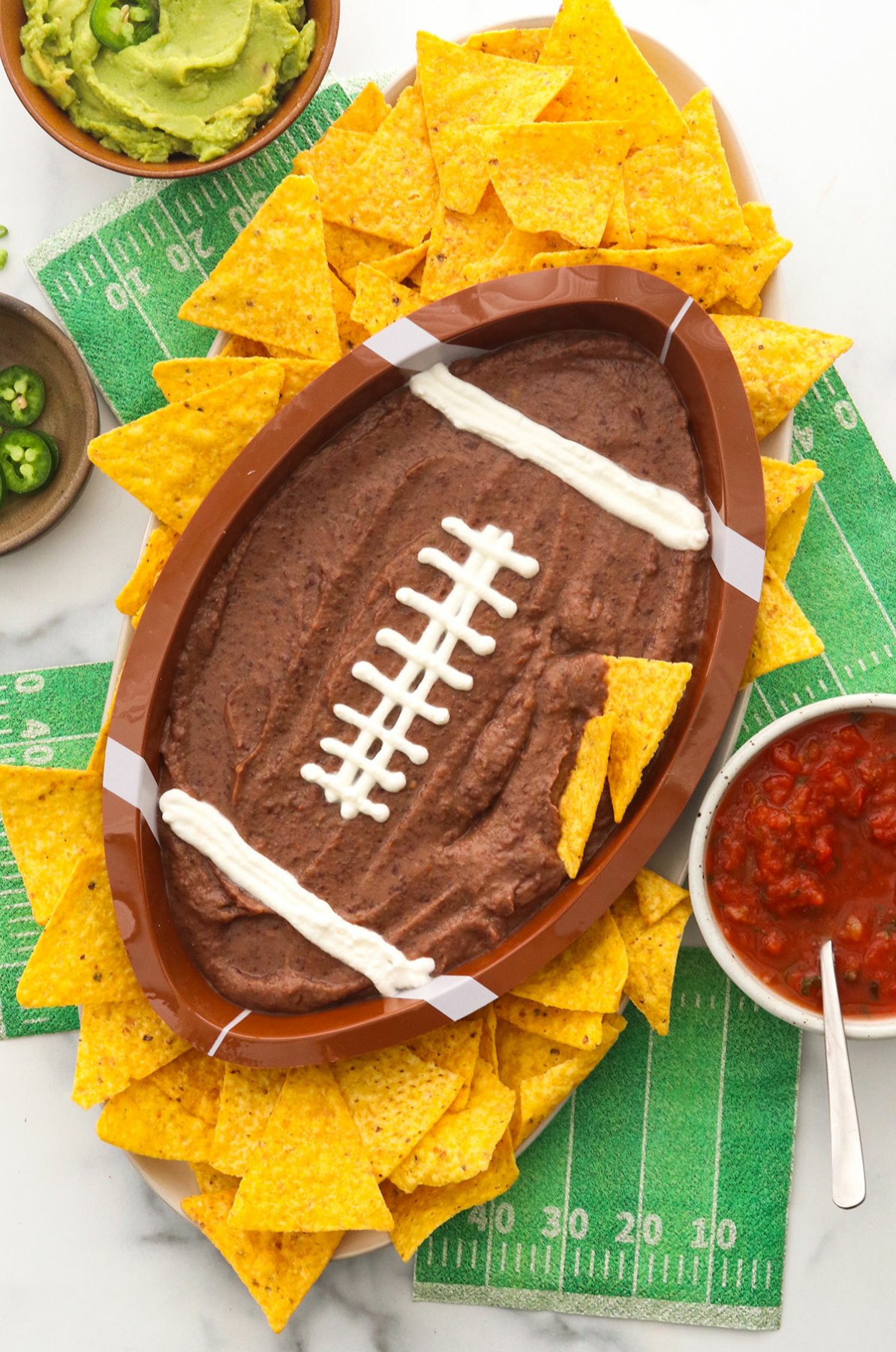 Black bean dip in a football shaped bowl with tortilla chips.