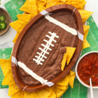 Black bean dip in a football shaped bowl with tortilla chips.
