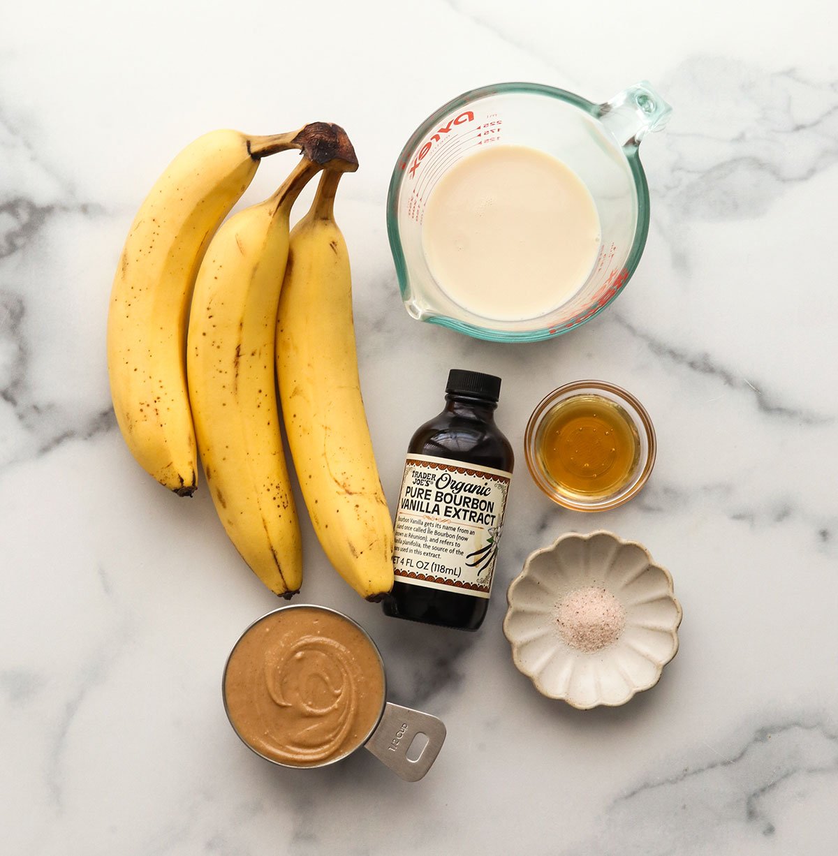 bananas, milk, vanilla, peanut butter, honey, and salt on a marble surface.