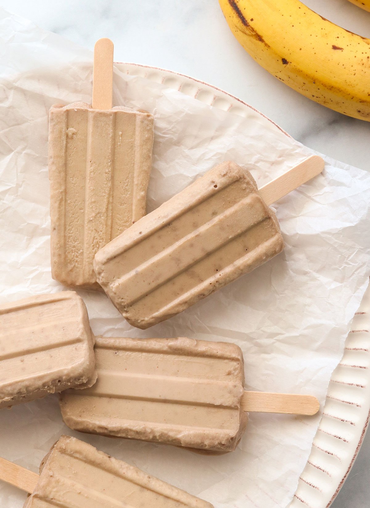 banana popsicles on a parchment lined plate.