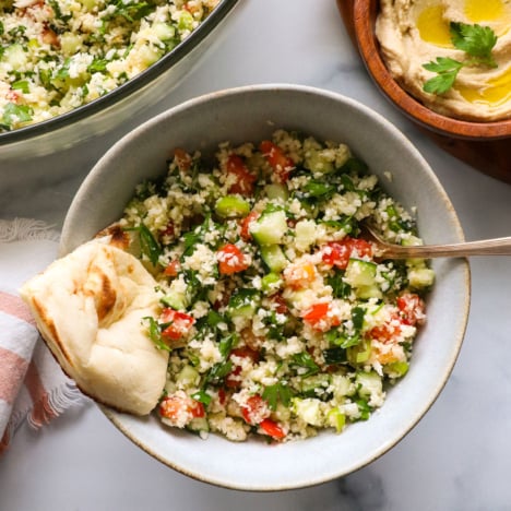 cauliflower tabbouleh served in a bowl with naan bread and hummus.