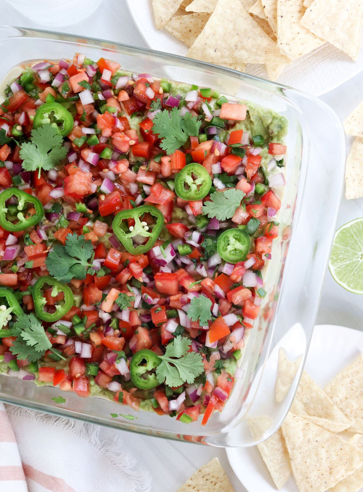 vegan 7 layer dip in glass dish served with chips.
