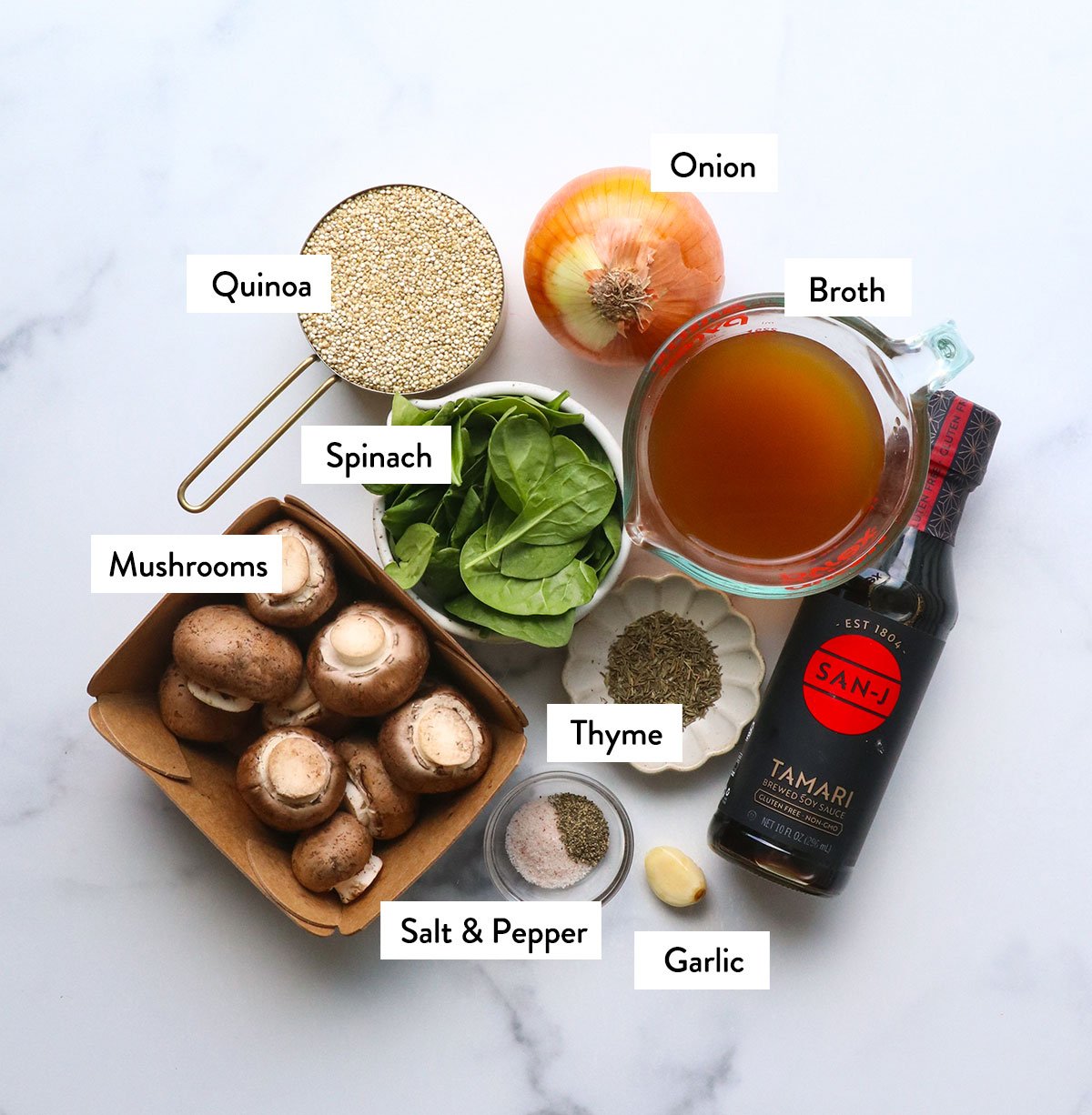 Mushrooms, quinoa, spinach, onion and spices marked on a white surface.