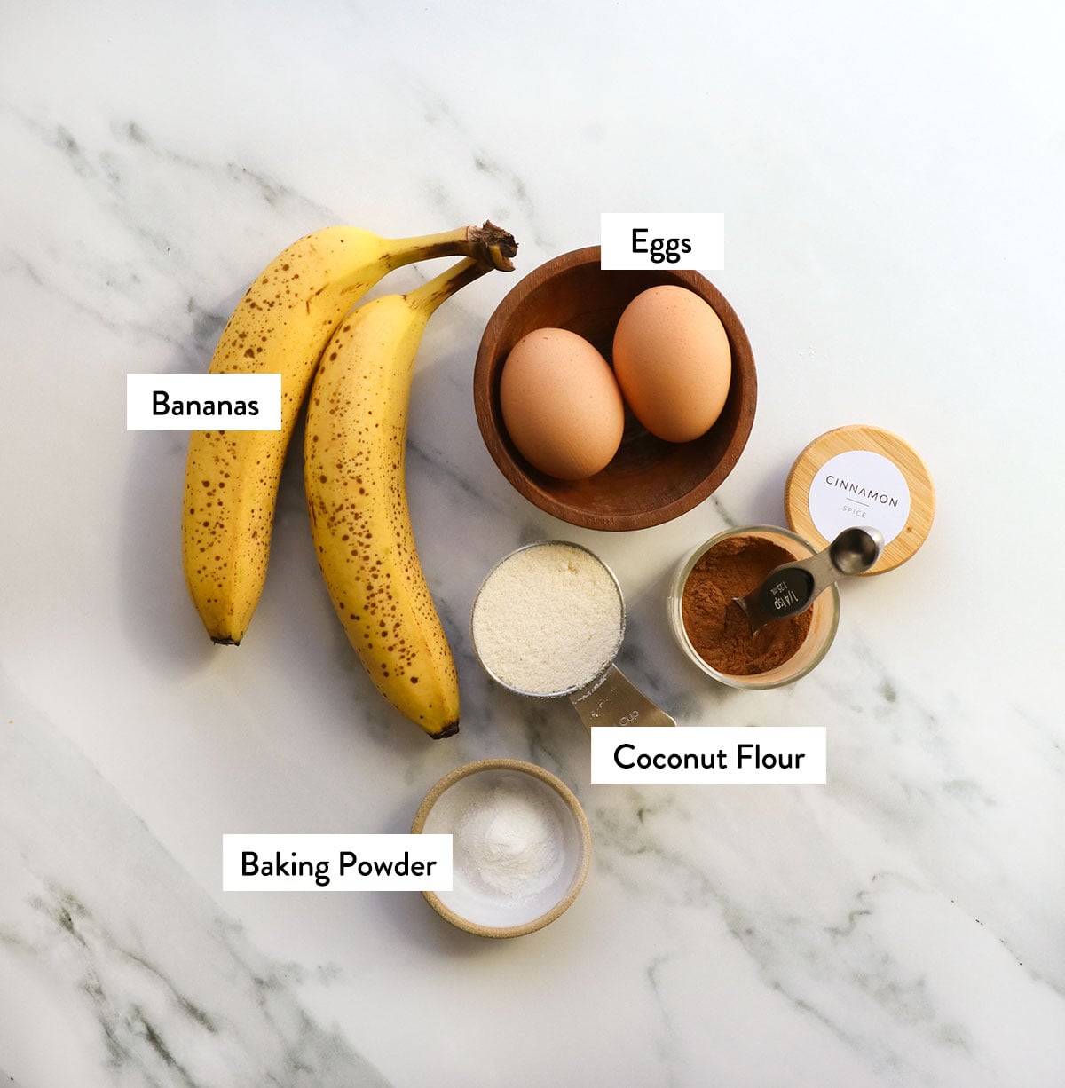 flour, bananas, eggs, baking powder, and cinnamon labeled on a white surface.