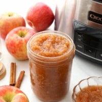 slow cooker applesauce stored in a glass jar near apples.
