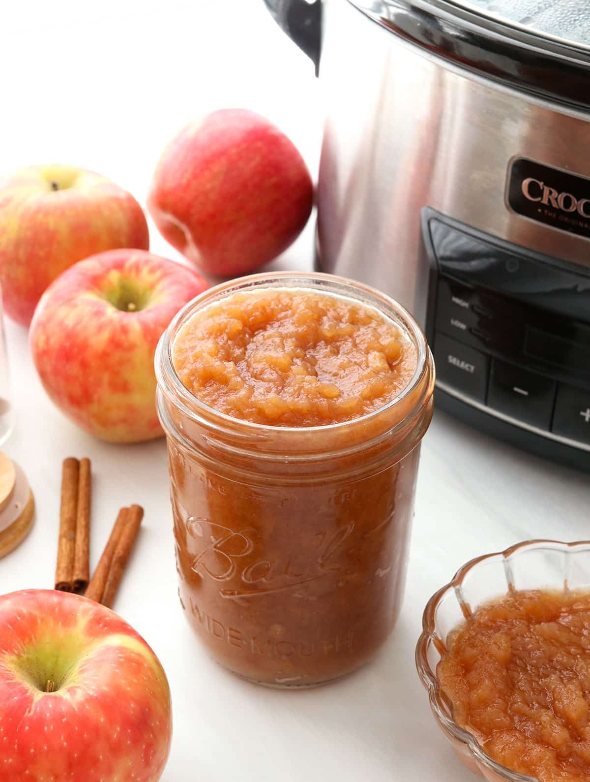 slow cooker applesauce stored in a glass jar near apples.