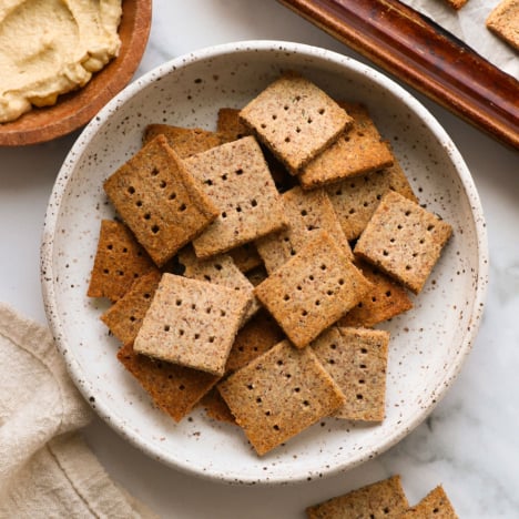 almond pulp crackers in a white bowl near hummus for serving.