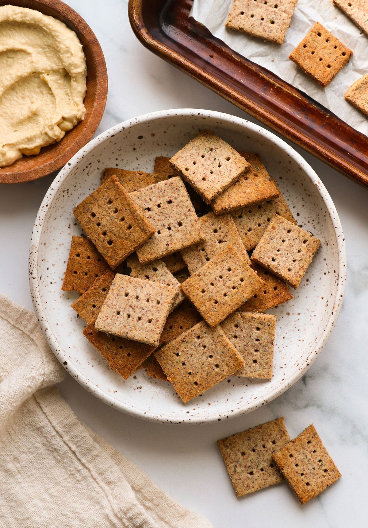 almond pulp crackers in a white bowl near hummus for serving.
