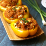 Three quinoa stuffed peppers on a wooden plate