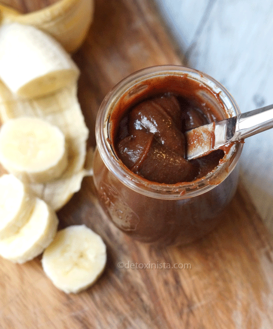 chocolate almond butter in a glass jar with a knife in it and sliced banan next to the jar