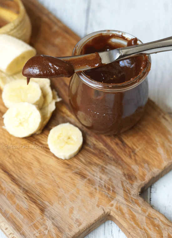 homemade chocolate almond butter in a glass jar and on a knife with banana slices next to it