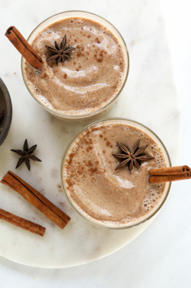 two glasses of chai smoothies with cinnamon sticks inside.