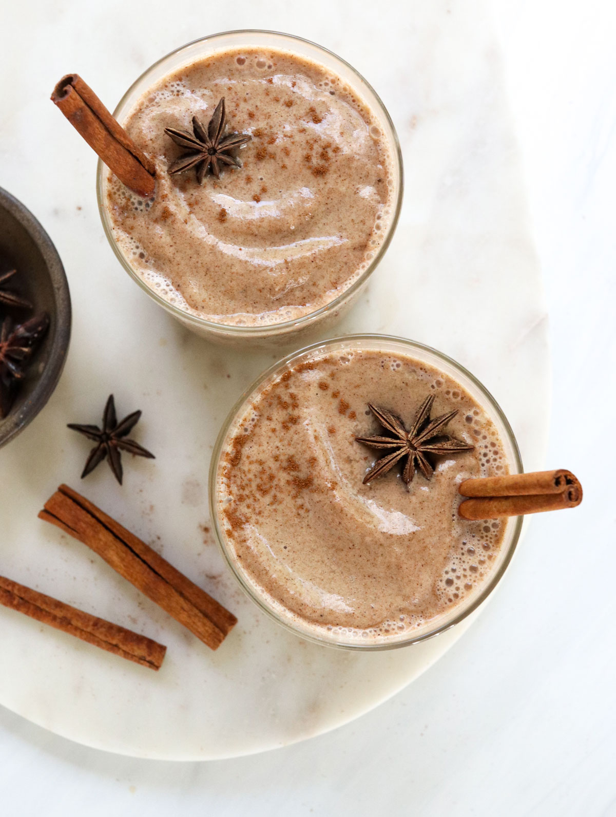 two glasses of chai smoothies with cinnamon sticks inside.