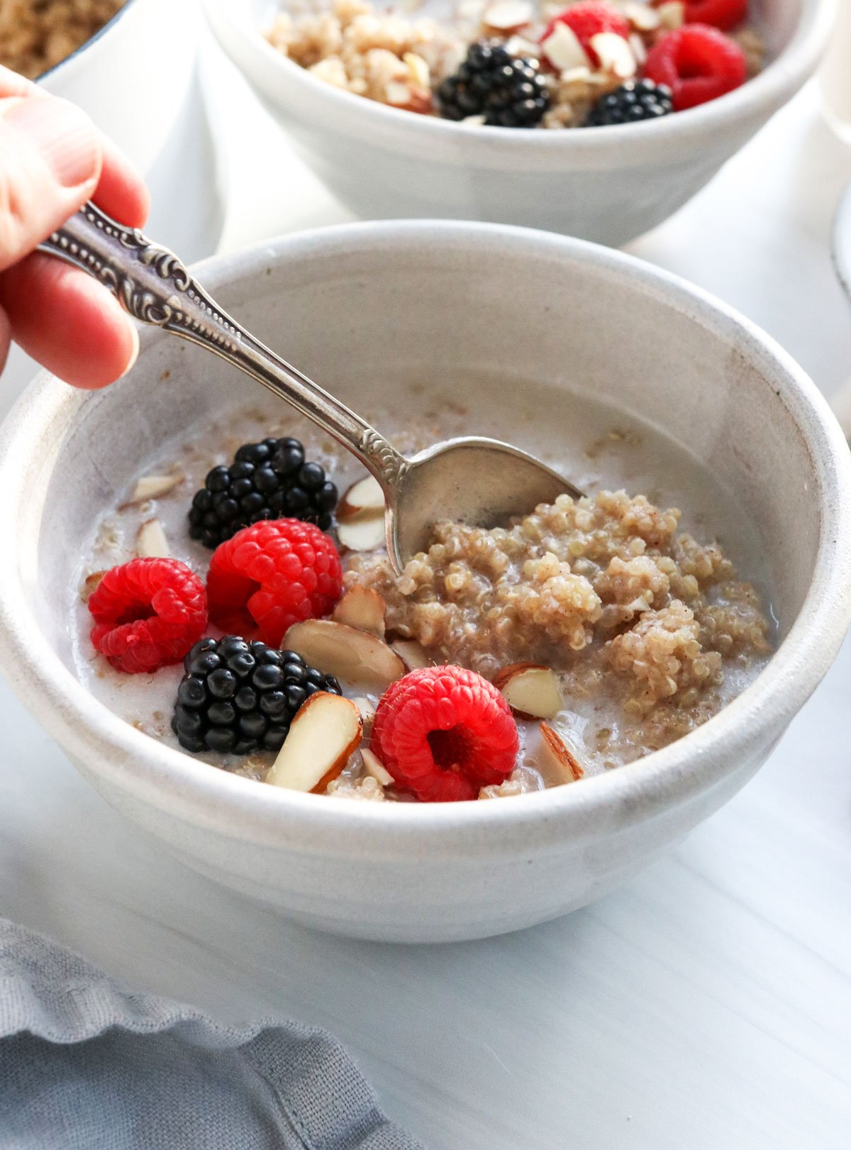 a spoon lifting up some quinoa porridge from a bowl with fruit.