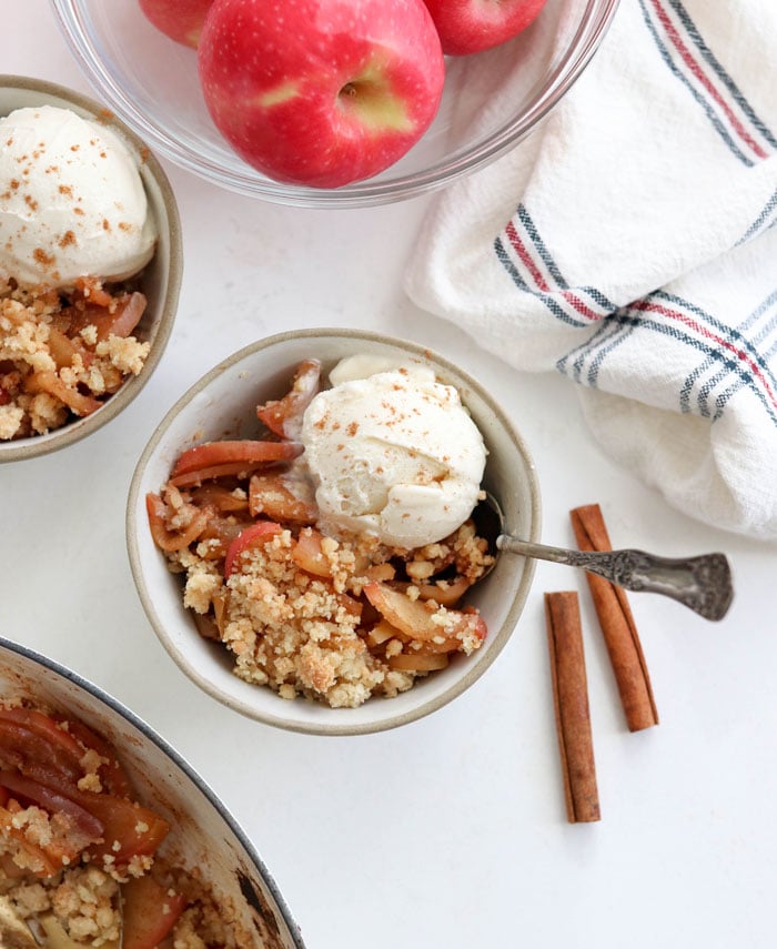 paleo apple crisp in a bowl with ice cream and cinnamon sticks