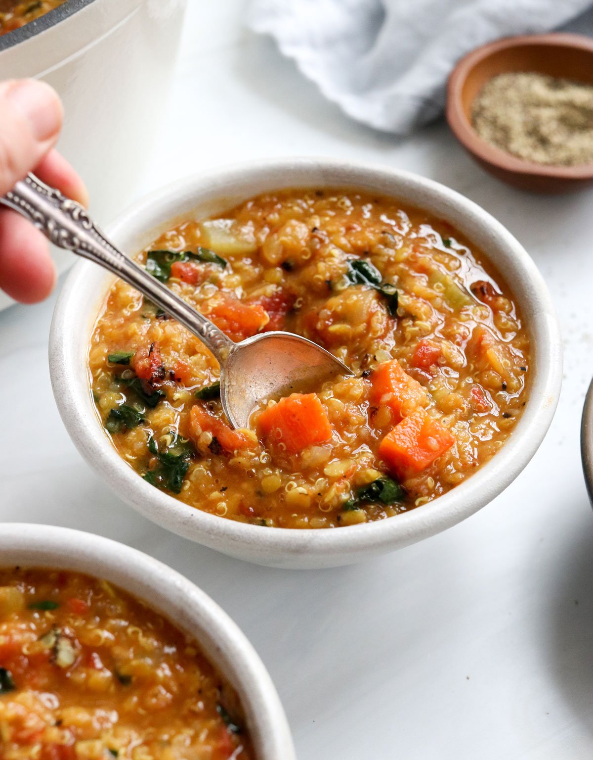 A spoon lifting up some quinoa soup from the bowl.
