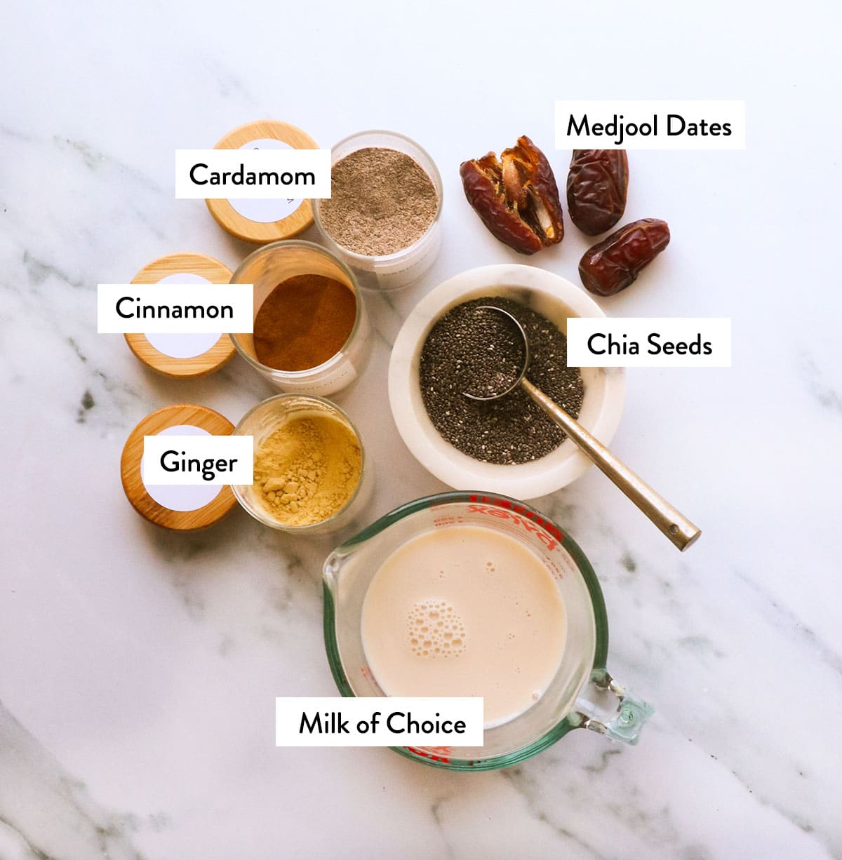 bowls of milk, chia seeds, ginger, cinnamon, and cardamom on a white surface.