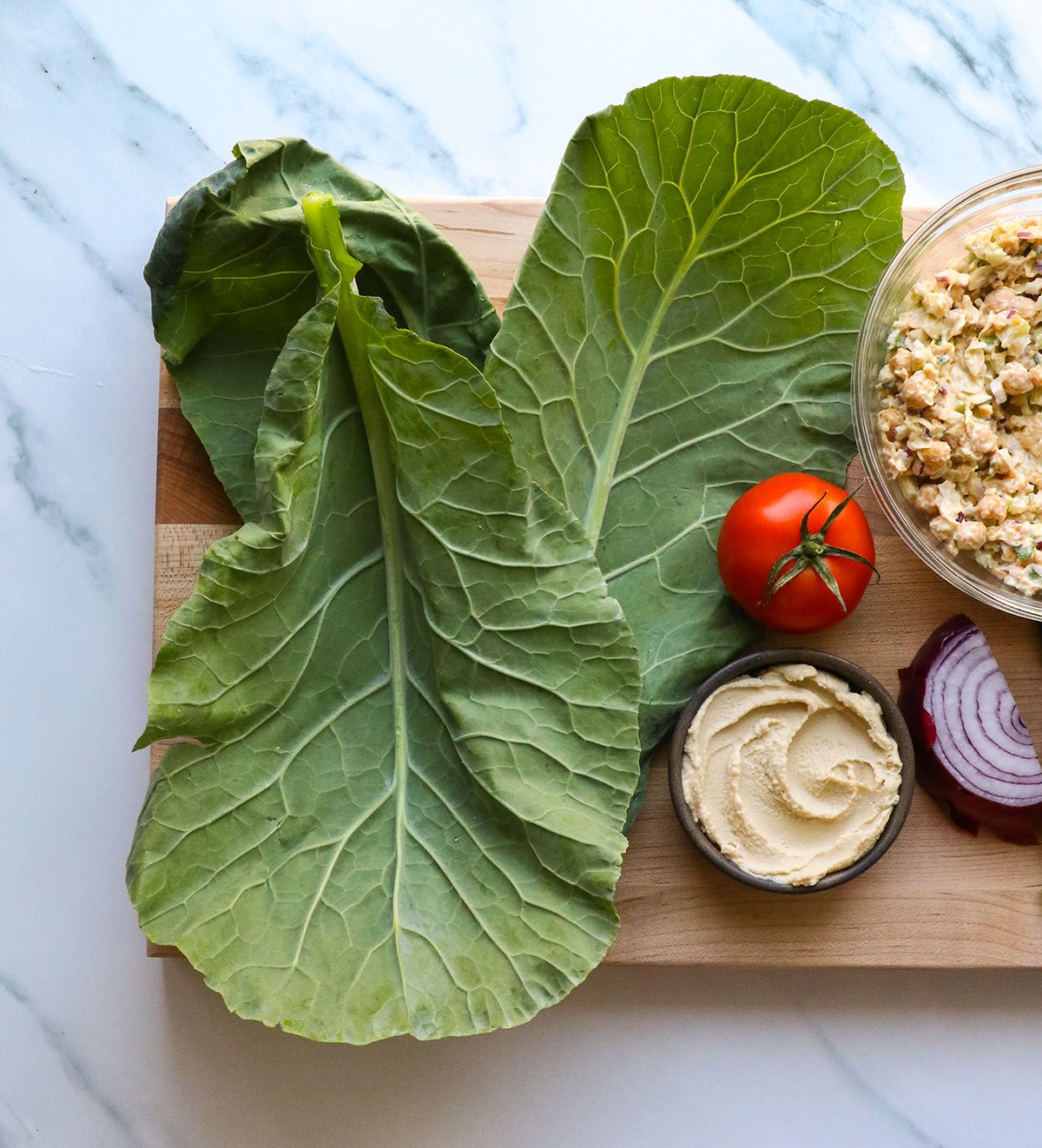 collard leaves on a cutting board with tomato and hummus.