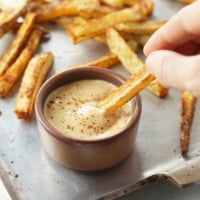 hand dipping french fry in vegan special sauce