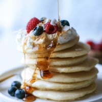 stacked pancakes with maple syrup being poured on it