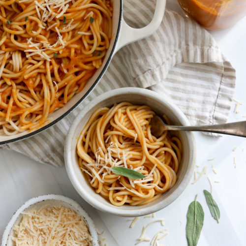 bowl of pumpkin pasta next to a white skillet