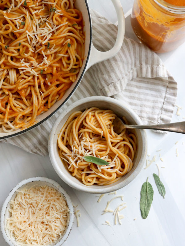 bowl of pumpkin pasta next to a white skillet