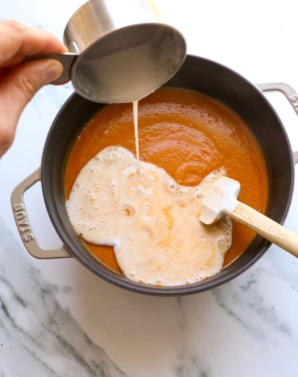 coconut milk poured into the pot of pumpkin tomato soup.