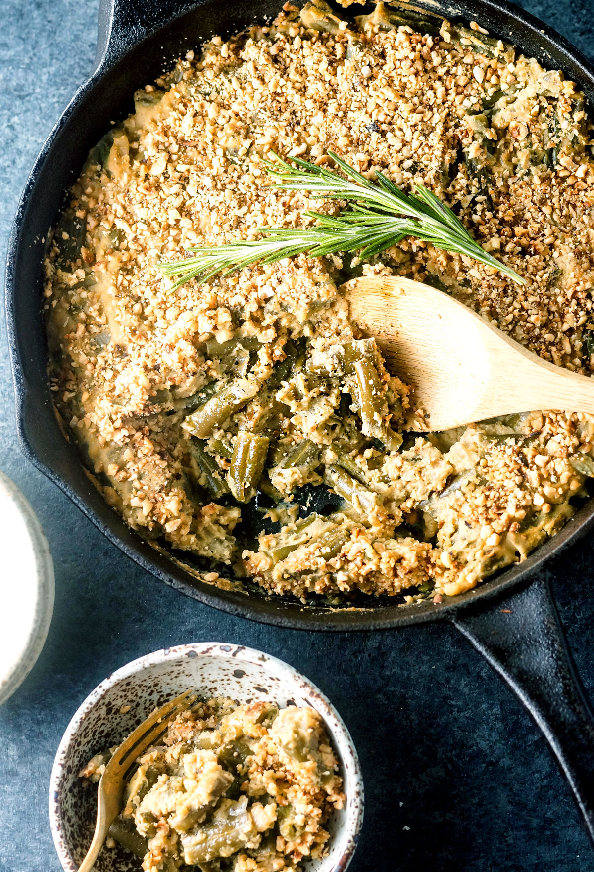 green bean casserole in a skillet with a wooden spoon scooping some out